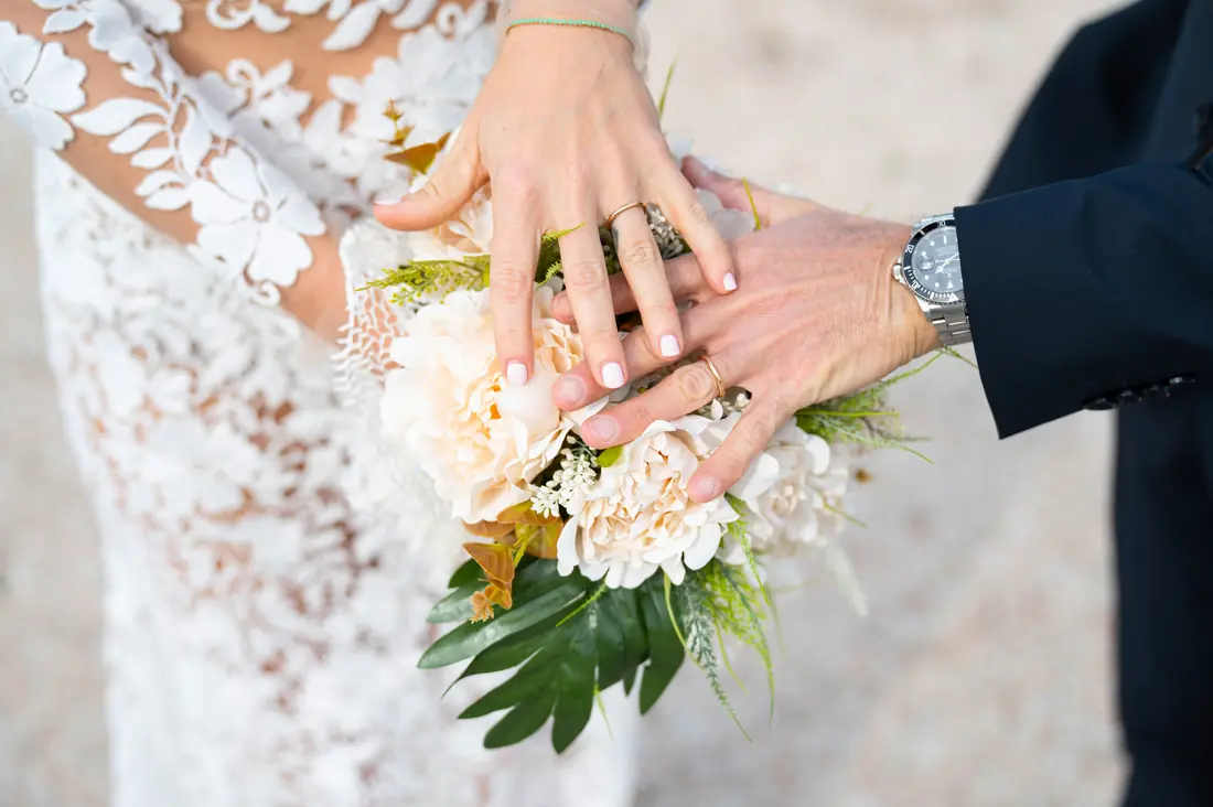 The couple’s hands with wedding rings and bouquet